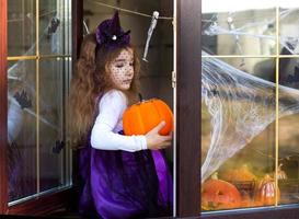 A girl in a witch costume on the windowsill by the window at a Halloween party, decorating the house cobwebs, bats, spiders, pumpkins. Terrible scenery, fear and horror photo