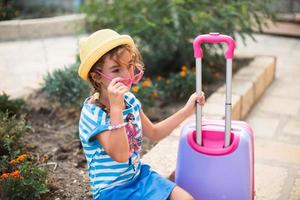 A girl with a suitcase, a hat and sunglasses is going on vacation. Waiting for the trip, arrival at the place of residence at the hotel. photo