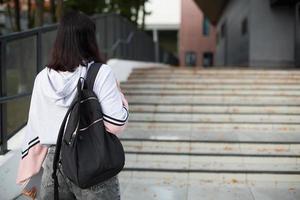 A female student with a black backpack and a notebook in her hands stands on the steps in front of the Institute. Higher education, the beginning of the school year, back to school. Copyspace photo