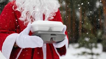 Food delivery service containers in hands of Santa Claus outdoor in snow. Christmas eve promotion. Ready-made hot order, disposable plastic box. New year holidays catering. Copy space, mock up photo