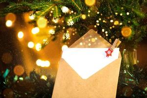 Envelope with sheet of paper- letter to Santa Claus, Copy space on a Christmas background of defocus lights in bokeh, garlands, fir branches. Clothespin-star. New year, wish list, dream, gifts photo