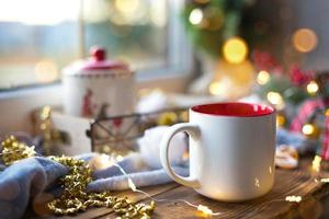 Christmas decor by the window on a cozy wooden windowsill with a mug with a drink and a cookie jar. Fairy lights, Christmas tree branch, breakfast tray still life photo