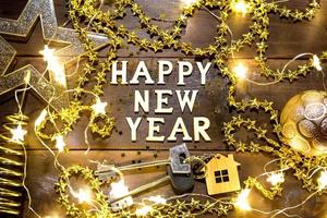 House key with keychain cottage on a festive background with sequins, stars, lights of garlands. Happy New Year-wooden letters, greetings, greeting card. Purchase, construction, relocation, mortgage photo