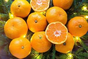 Fresh tangerines in garland lights, on fir branches and tinsel - new year's bright background. Half of an orange, citrus aroma of the holiday. Christmas, New year. Space for text. photo