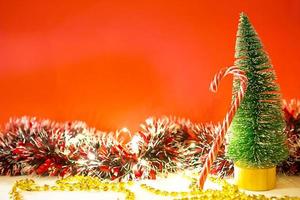 Christmas tree on a red background with lights of garlands, caramel striped cane, Santa hat, tinsel. New year, festive atmosphere. Copy space photo