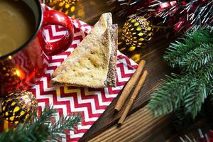 Triangular cookies with powdered sugar and cinnamon on a napkin with a zigzag pattern in the Christmas decor. Red coffee mug with marshmallow, spruce branches, garland, new year, comfort. photo