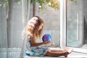 The girl on the window of the house is holding a lamp in the shape of a planet, a globe. Peace, ecology, environment, peaceful photo