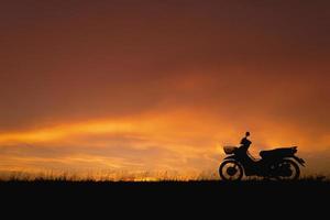 cielo naranja del atardecer. motocicleta de silueta en el paisaje de puesta de sol como telón de fondo foto