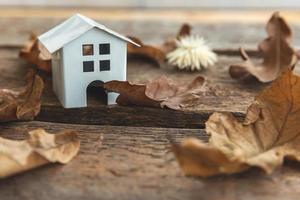 Autumnal Background. Toy house and dried fall leaves on wooden background. Thanksgiving banner copy space. Hygge mood cold weather concept. Hello Autumn with family. photo