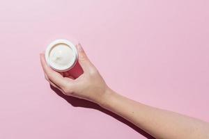 Woman Hand holding an open cosmetic cream container on pink background. Mockup with space for text. Branding presentation of cosmetic product photo