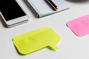 closeup of white office desk, two colored stickers for notes, smartphone, notebook and metallic pen, business mockup photo