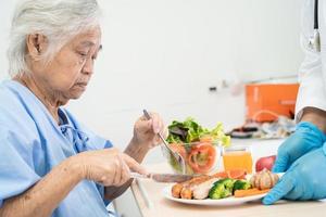 Asian senior or elderly old lady woman patient eating breakfast and vegetable healthy food with hope and happy while sitting and hungry on bed in hospital. photo