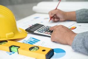 Asian engineer with plan project blueprint, graph and yellow helmet and engineering construction tools. photo