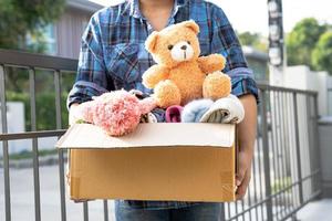 Holding clothing donation box with used clothes and doll at home to support help for poor people in the world. photo