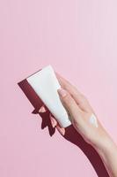 Woman's hand with a tube and a swatch of cream on a pink background. Cosmetic products concept. Copy space. Hard shadows photo