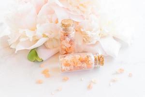 Beauty and spa concept. Pink himalayan salt close-up in glass botles, essential oil and peony flower in the background. Selective focus photo