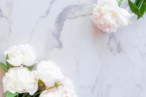 Template for a romantic greeting card with creamy peonies on a white marble background. Blossoming flowers on a white background. pink peonies on a white marble table, flat lay photo