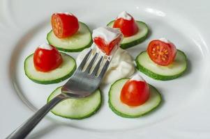 tomates cherry y pepinos en rodajas con salsa mayonesa en un plato. ensalada fresca foto