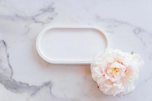 Top view of empty concrete tray with peony flower on marble table. Mockup presentation for goods or cosmetics. photo