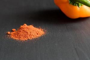 orange bell pepper and paprika powder on black background, copy space for your text photo