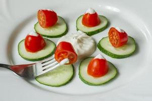 tomates cherry y pepinos en rodajas con salsa mayonesa en un plato. ensalada fresca foto