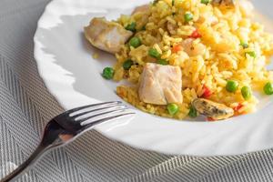 paella with chicken and seafood on white plate. Spanish dish served on table photo