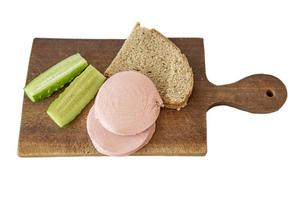 rye bread, cucumber and sausage on brown wooden desk on white background