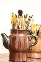 Brushes of the artist in clay pitcher on wooden shelf photo