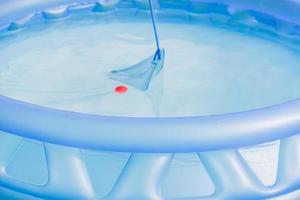 cleaning of garden swimming pool . Boy tries to cach red ball with Skimmer net photo