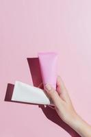 Revitalizing hand cream for healing, soften and recovery. Young woman hand holding two tubes of moisturizing lotion. Copy space, close up, pink background, flat lay, top view. photo