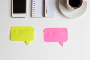 top view of white office desk, two colored stickers for notes, smartphone, notebook with metallic pen and cup of black coffee, business mockup photo