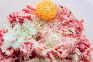 Minced meat in a bowl with raw egg, spices and chopped onion for cooking cutlets, selective focus photo