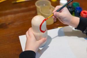 little boy paints russian nesting doll called matrioshka with red paint photo