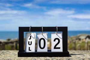 Jul 02 calendar date text on wooden frame with blurred background of ocean. photo