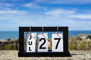 27 de julio texto de fecha de calendario en marco de madera con fondo borroso del océano. foto