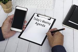 Businessman writing Today's Meeting Agenda with holding a smartphone. photo