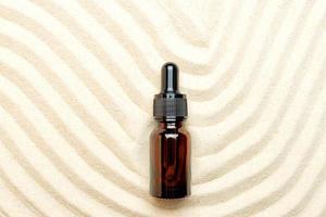 Serum or liquid collagen dropper bottle on sand background. Anti age cosmetics products. Skin care beauty, summer concept. zen style with vawes on sand. Above view, Natural beige color photo