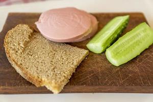 pan de centeno, pepino y salchicha en un escritorio de madera marrón foto