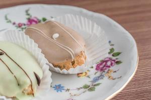 eclairs franceses en plato de porcelana de colores sobre mesa de madera. foto