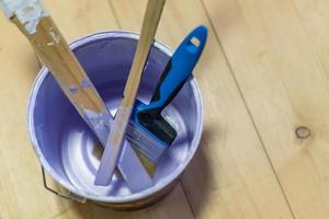 empty paint can with wooden sticks and paint brush on wooden floor photo