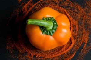 orange bell pepper and paprika powder on black background, top view photo