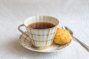 taza de té negro con galleta crujiente sobre mantel de algodón blanco foto