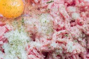 Minced meat in a bowl with raw egg, spices and chopped onion for cooking cutlets, selective focus photo