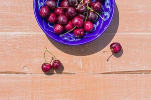blue plate of ripe sweet cherry on wooden table photo