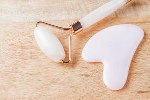Gua Sha massager and rose quartz massage roller on wooden background. Pink jade stone for face and body care. Horizontal shoot. Flat lay, top view. Copy space for your text photo