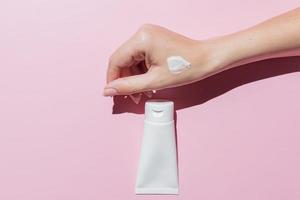 Female hand applies cosmetic skin care moisturizer cream on a skin on pink background. Cosmetic mockup for designers photo