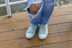 mujer en elegantes jeans rasgados azules con zapatillas de menta. mirada de la moda de la calle. piernas de una niña en el pavimento. foto