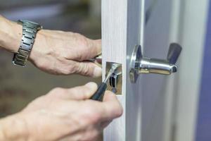 hombre reparando el pomo de la puerta con destornillador. mano del trabajador instalando un nuevo casillero en la puerta foto