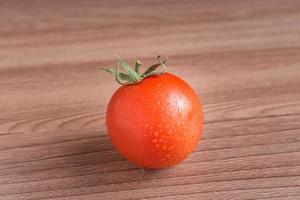 tomate rojo con gotas de agua sobre fondo de madera foto