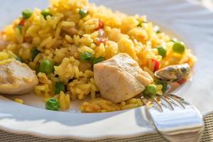 paella with chicken and seafood on white plate. Spanish dish served on table photo